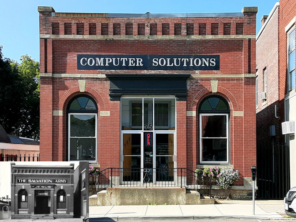 A red brick building labeled "Computer Solutions," featuring arched windows, a centered entrance with steps, and planters with flowers on either side.